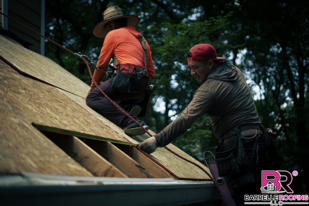 A roofer measures a section of a roof as new plywood is prepared to be installed