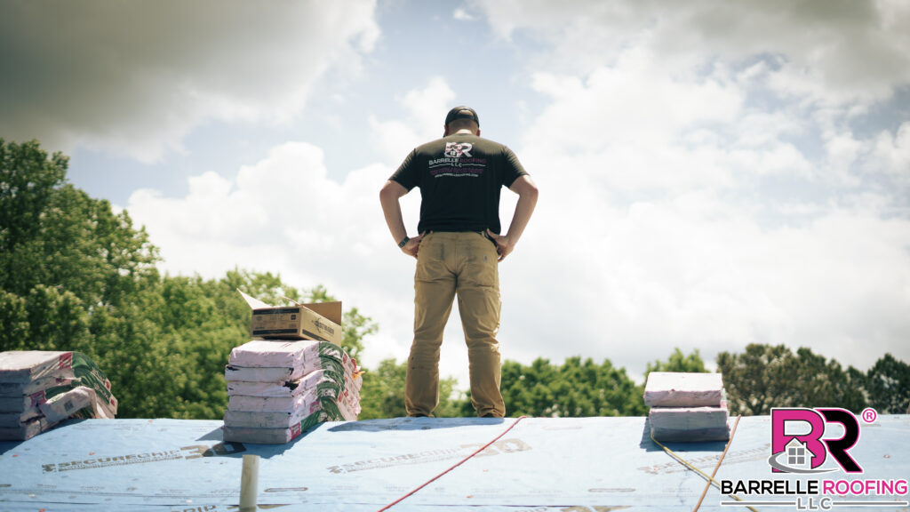 A roofing specialist stands on the ridge of a roof as new shingles are being installed